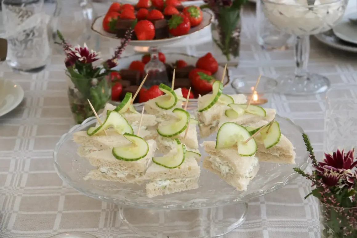Smörgåsar med gurka och krämig fyllning, perfekta för ett afternoon tea recept. Jordgubbar och choklad i bakgrunden.